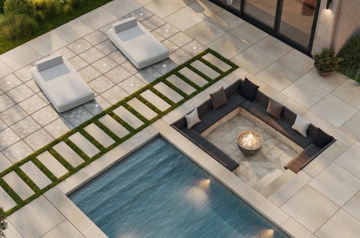 Close up view of an outdoor seating area featuring a sunken firepit, pool and patio chairs.