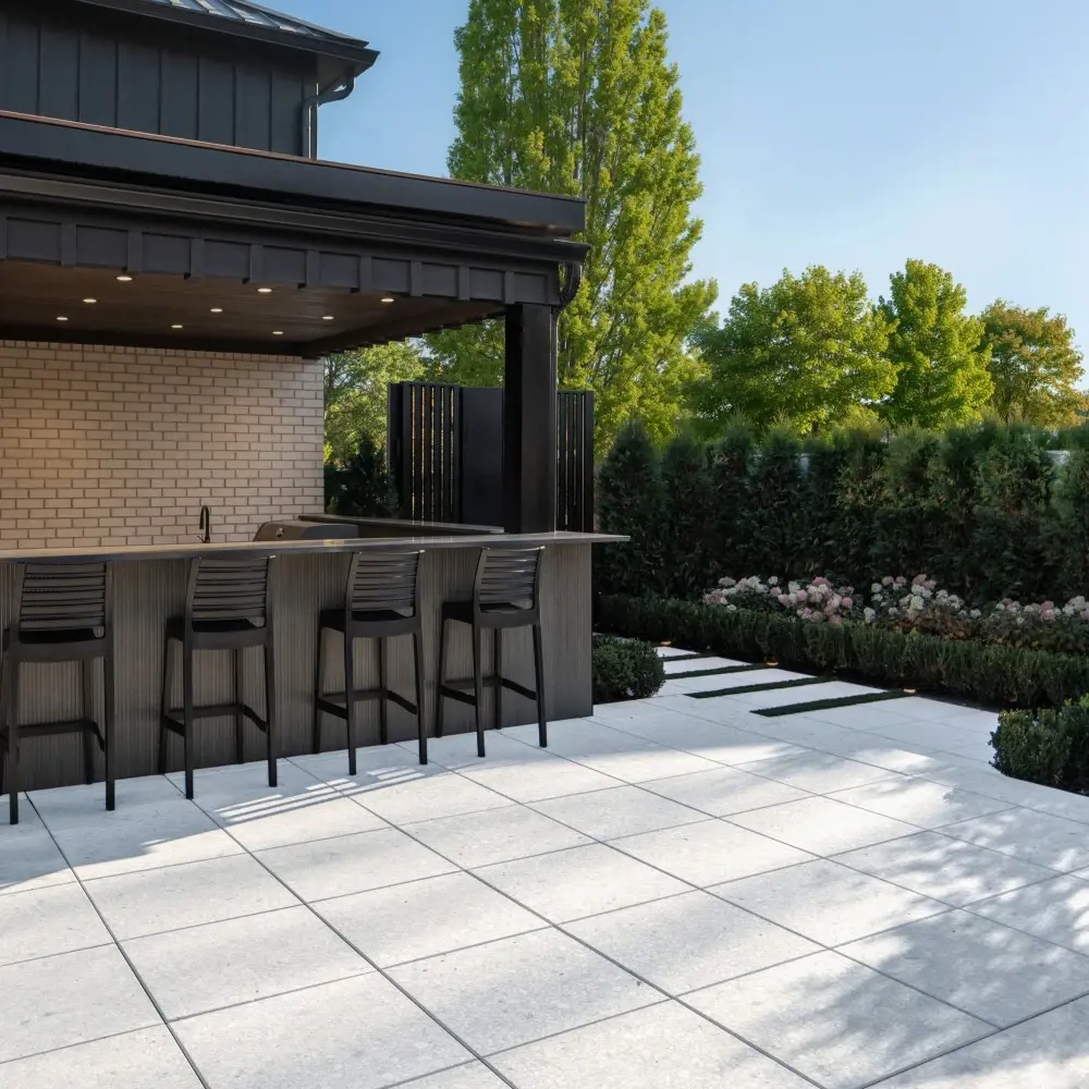 Outdoor kitchen patio with Terrazzo 600×600 concrete slabs in Mineral White, paired with clean-lined paving and landscaped edges.