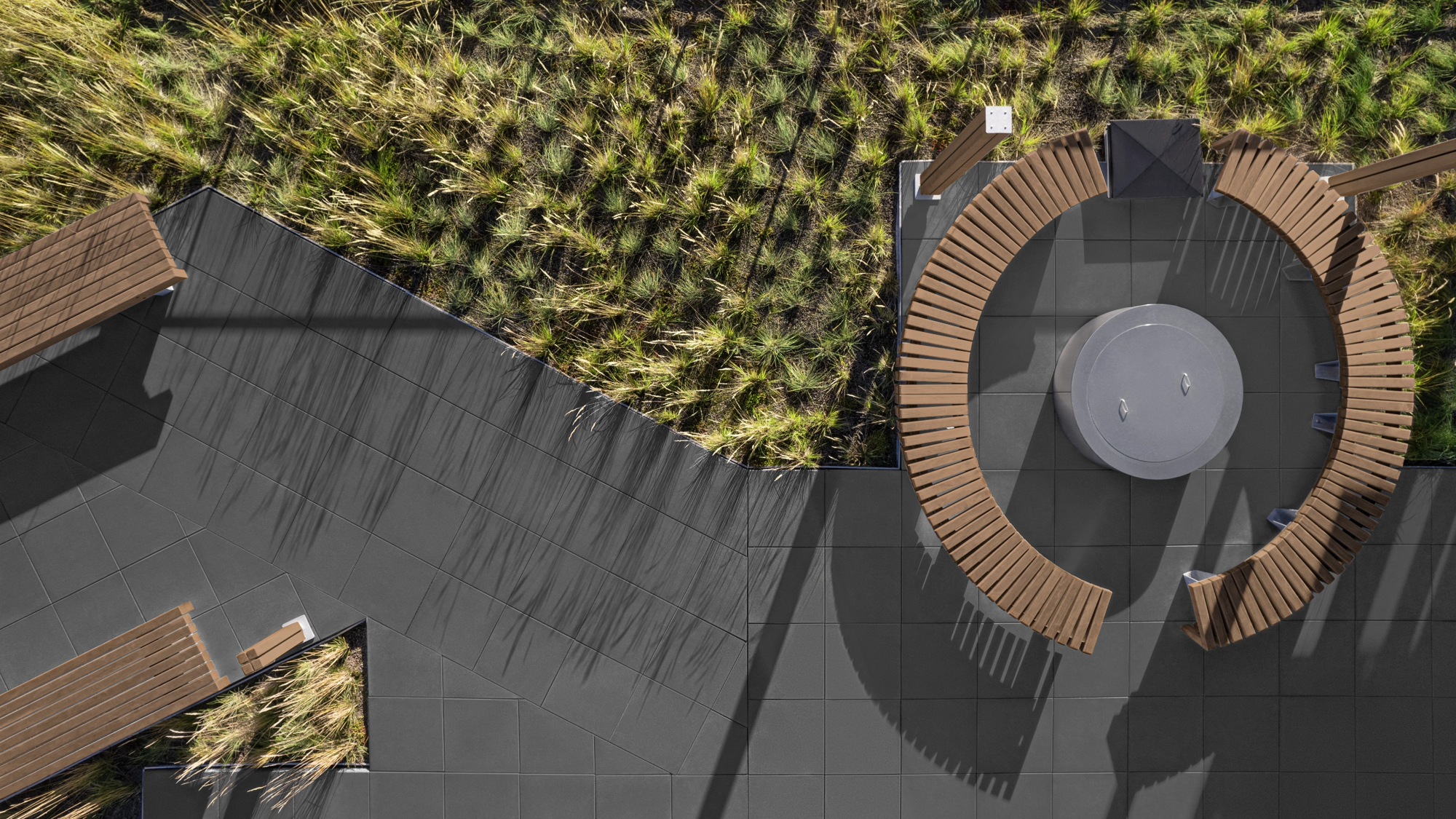 Bannière des études de cas Techo-Bloc avec un espace de vie extérieur moderne comprenant des dalles de pierre foncées, des sièges circulaires et de la verdure luxuriante.