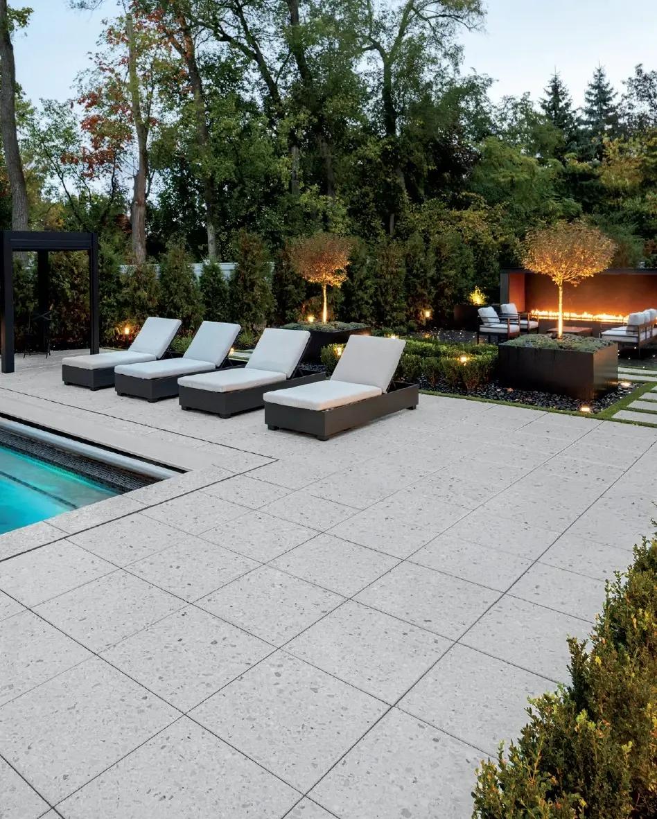 Poolside patio with light concrete pavers, lounge chairs, and integrated landscape lighting.