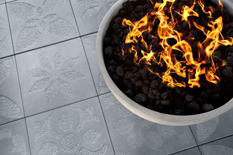 Un plan rapproché d'un plancher mettant en vedette les dalles commerciales Industria Flora de Techo-Bloc dans la couleur nickel grisé et le bol à feu Lumi à la droite.