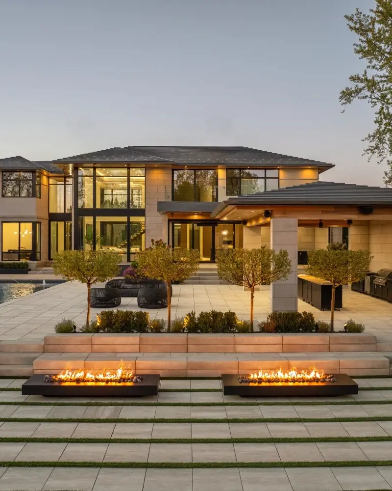 Contemporary backyard terrace featuring warm-toned paving, linear fire features, and layered landscaping for a welcoming outdoor atmosphere.
