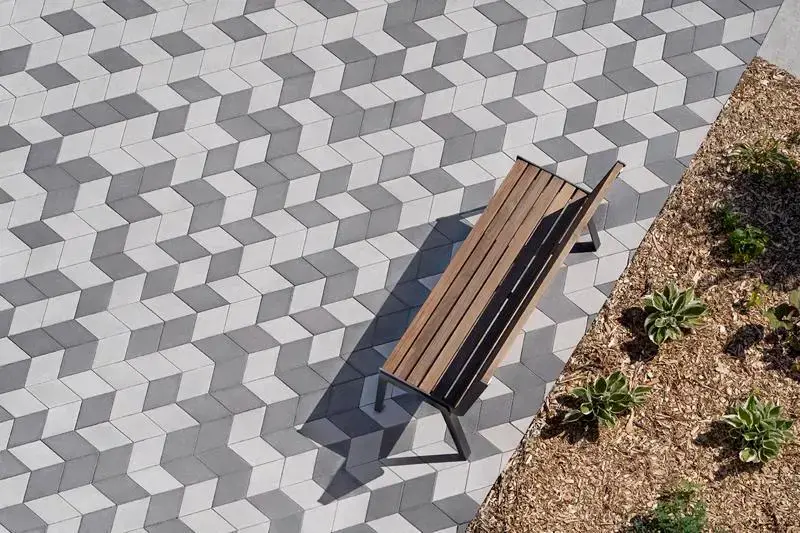 Outdoor seating area paved with Techo-Bloc pavers in a geometric cube pattern beside landscaped planting beds. 
