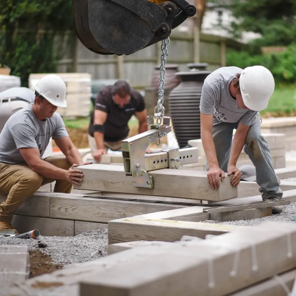 Entrepreneurs installant de grands pavés avec un équipement de levage sur un chantier, montrant le travail d’équipe et la précision.