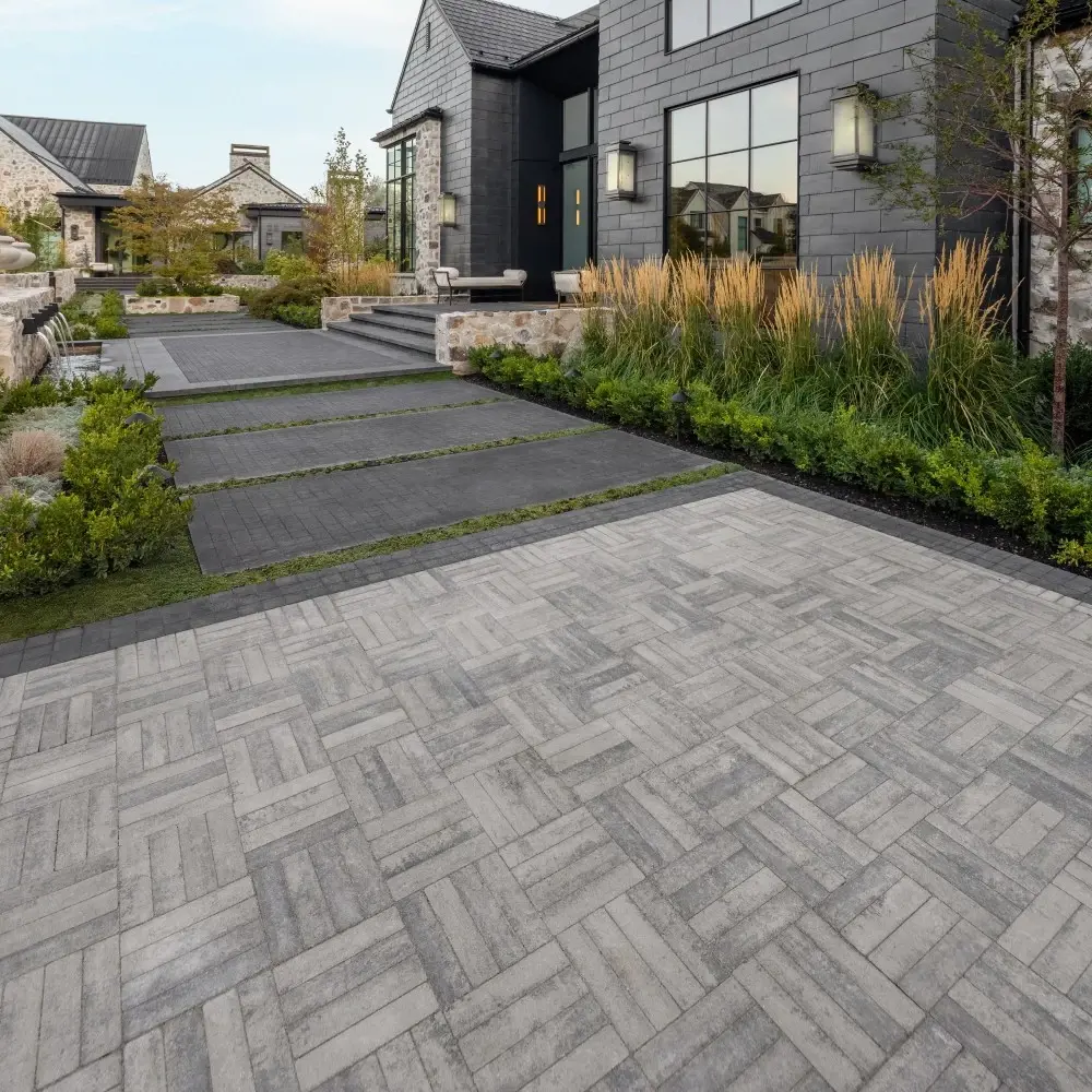 Residential entry terrace with Westmount concrete pavers in Shale Grey, laid in a herringbone pattern and framed by landscaped beds.