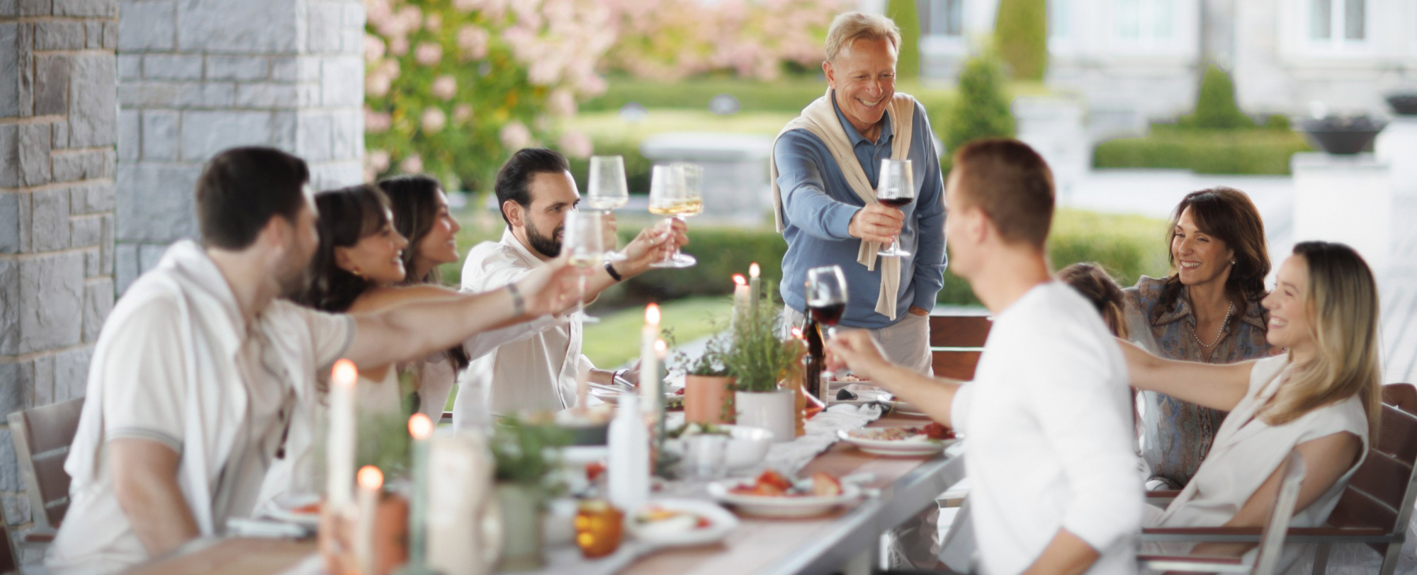 Groupe de personnes qui lèvent leur verre lors d’un souper extérieur sur un patio en pierre, dans une ambiance chaleureuse et accueillante.