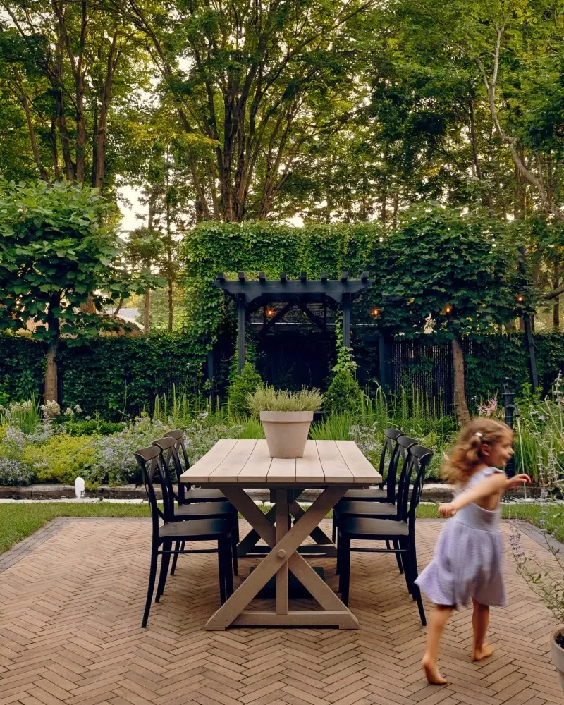 Outdoor dining patio surrounded by lush greenery, featuring warm-toned pavers and an organic garden-inspired layout.