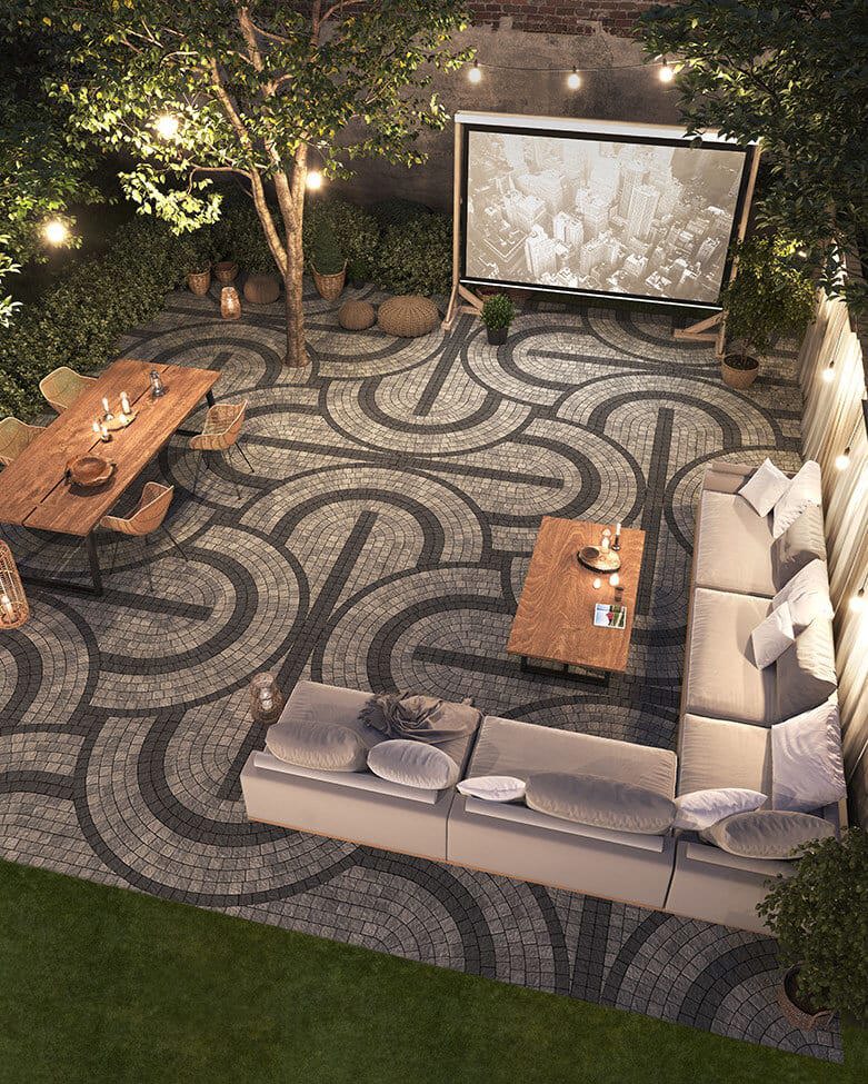 Areal view of a backyard featuring a firepit and patio designed with an intricate circular pattern using light and dark grey pavers. 