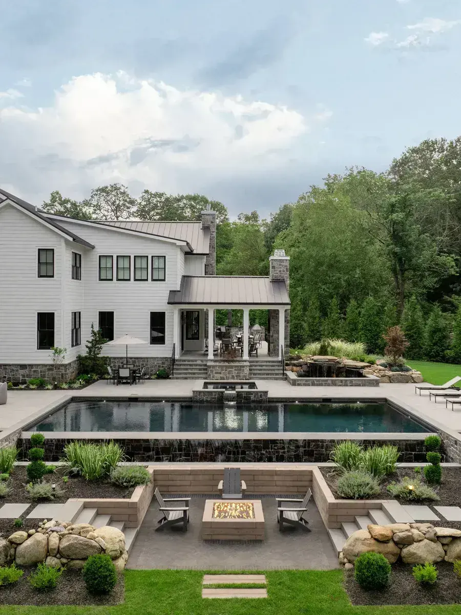 A luxurious backyard with a pool, fire pit, and garden, using Everest Slab in Greyed Nickel, Westmount Paver in Onyx Black, and Borealis Wall in Hazelnut Brandy.