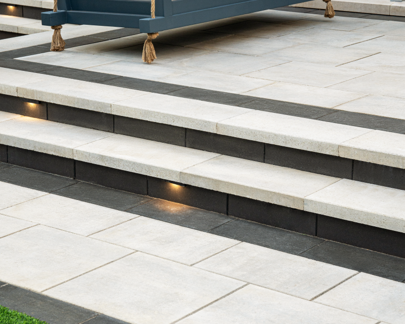 Raffinato steps with light concrete slabs, dark accent borders, integrated step lighting, and a modern patio swing area.