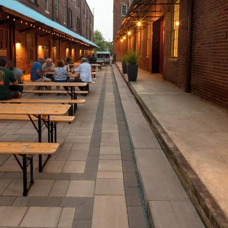 Cour extérieure pour repas et événements aménagée avec des pavés Blu 60 de Techo-Bloc, associés aux marches et murs Borealis, conçue pour la durabilité et la gestion efficace des eaux pluviales.