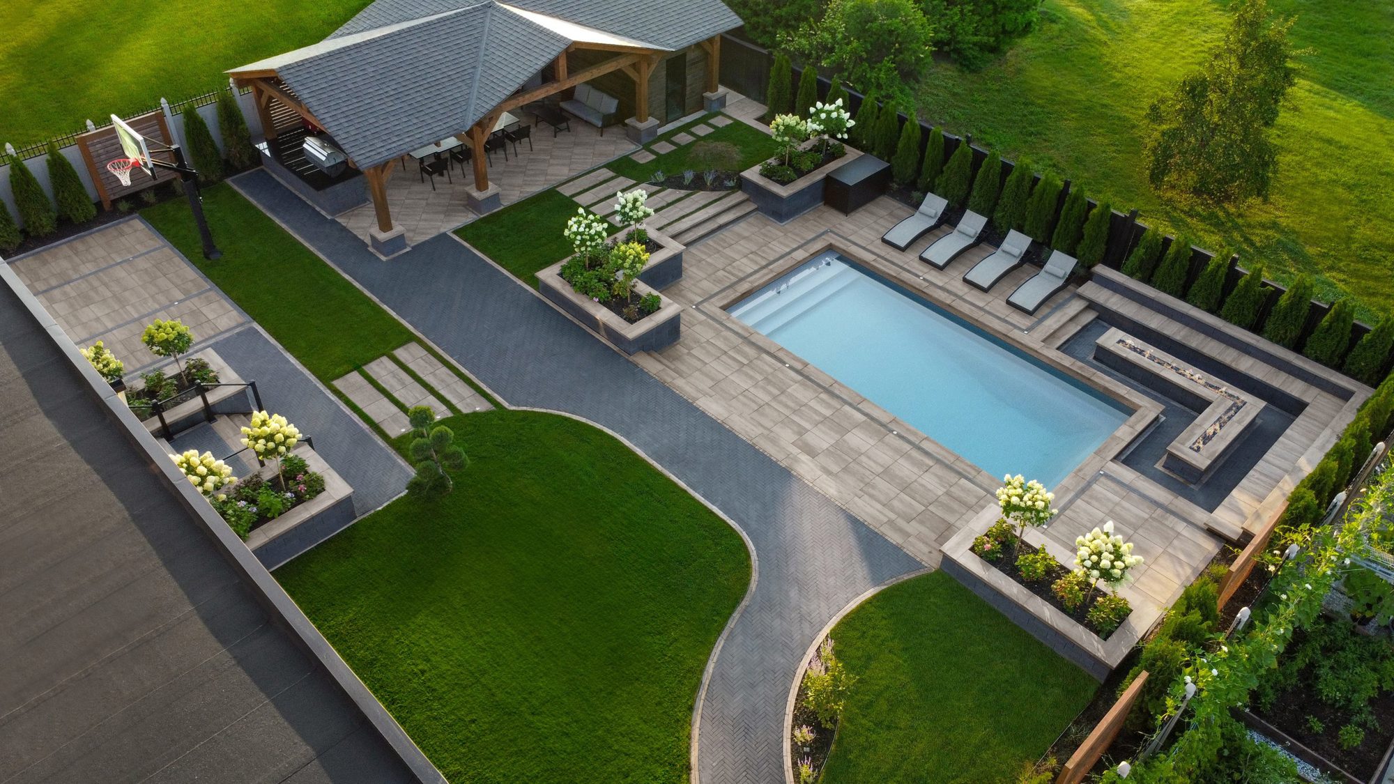 Aerial view of a modern backyard featuring a pool, lounge chairs, pergola, and clean geometric hardscaping.
