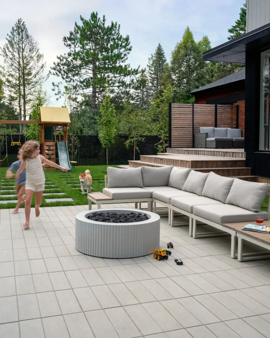 Contemporary backyard featuring a circular fire pit, modular outdoor seating, and light-toned paving designed for family relaxation and play.