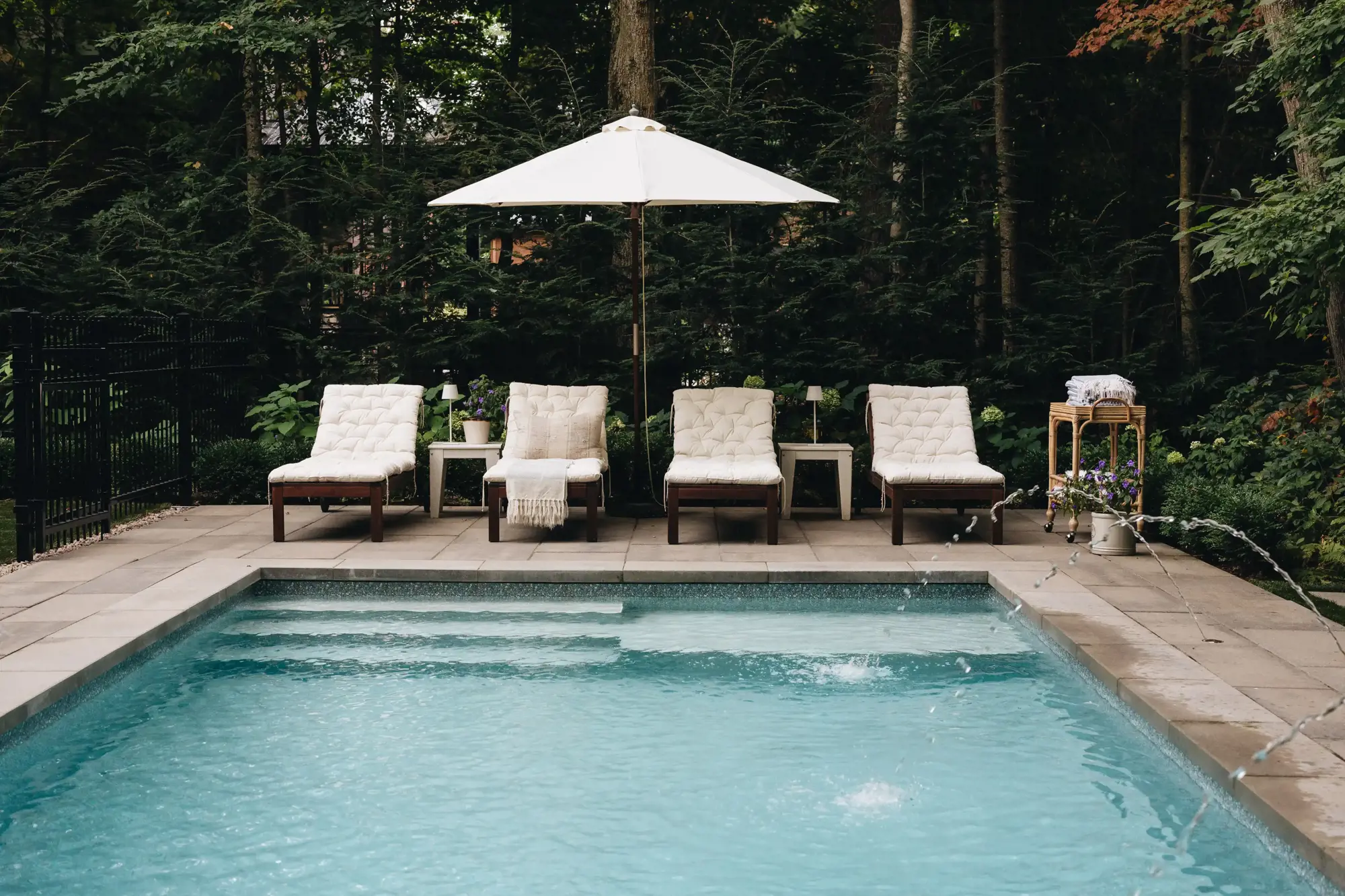 Quatre chaises longues et un parasol au bord de la piscine avec jets d'eau