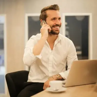 Person speaking on the phone while working on a laptop in a modern office.