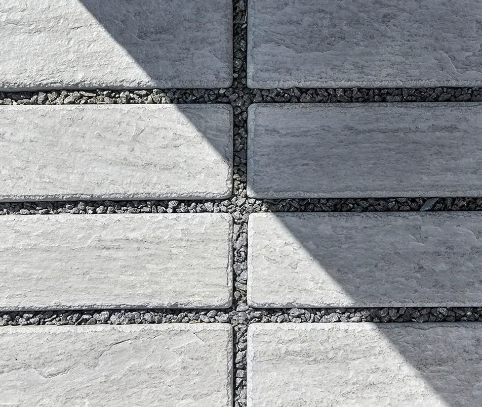 Gros plan du pavé Mika perméable en gris clair, avec texture lisse et joints remplis de gravier.