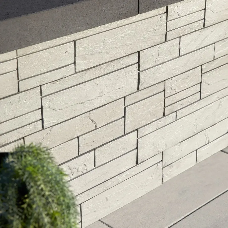 Un mur moderne avec un aspect pierre empilée, parfait pour les espaces extérieurs contemporains, utilisant le mur Iconic de Techo-Bloc dans des tons clairs.