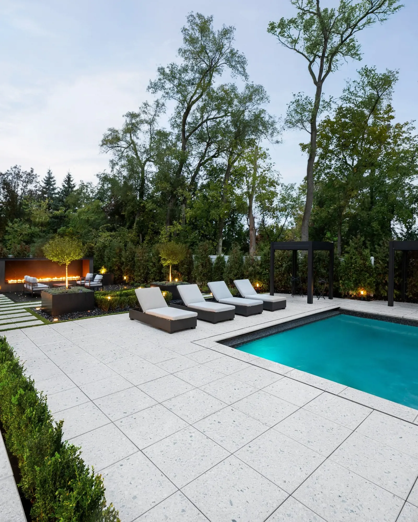 Poolside patio with Terrazzo concrete slabs, modern lounge seating, and integrated linear fire features.