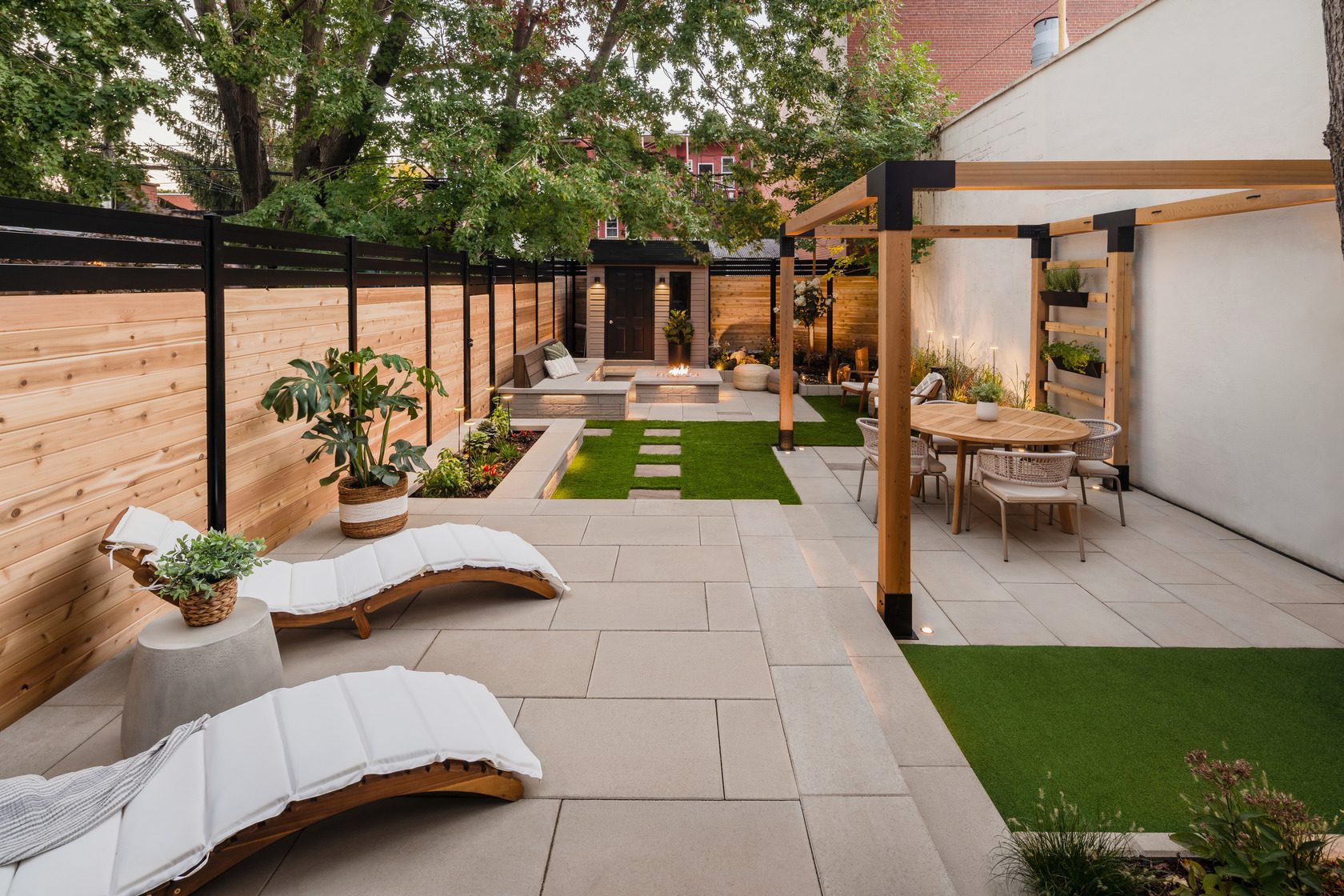 A backyard with lounge chairs, dining area, garden beds and firepit. 