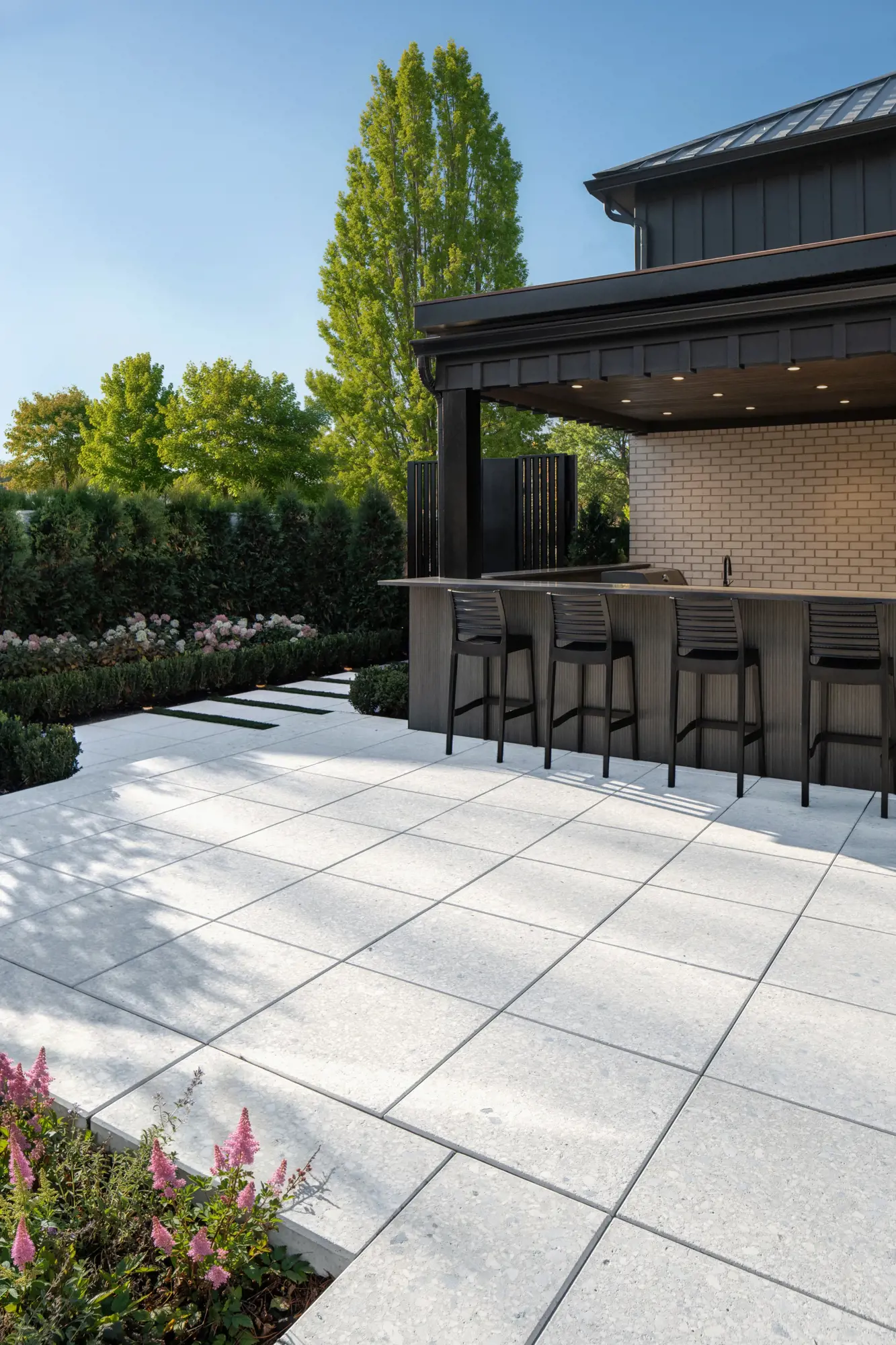 Bar de cuisine extérieure avec tabourets sur Terrazzo Blanc Minéral près d'un cabanon sombre