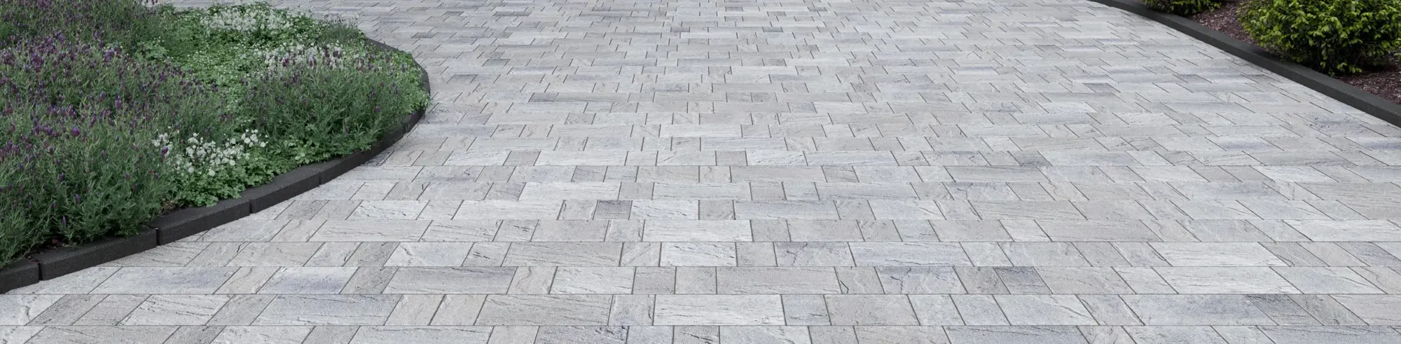 Eva Slate paver by Techo-Bloc in Shale Grey with slate texture, forming a curved driveway bordered by dense greenery.