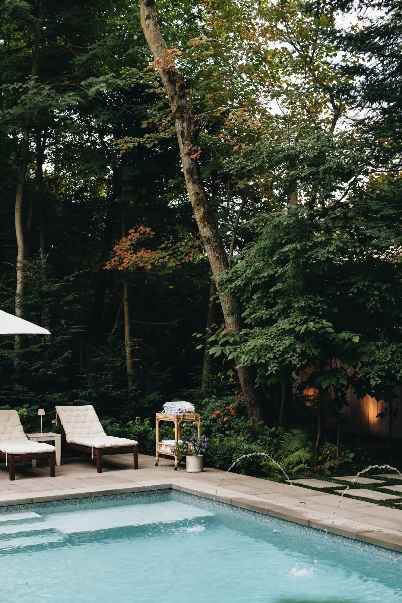 Coin de piscine avec chaises longues, jets d'eau et arbres matures
