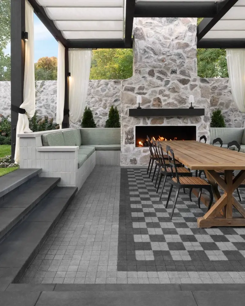 Modern outdoor living space with patterned concrete pavers, a stone fireplace, and dining area blending contemporary design with timeless character.