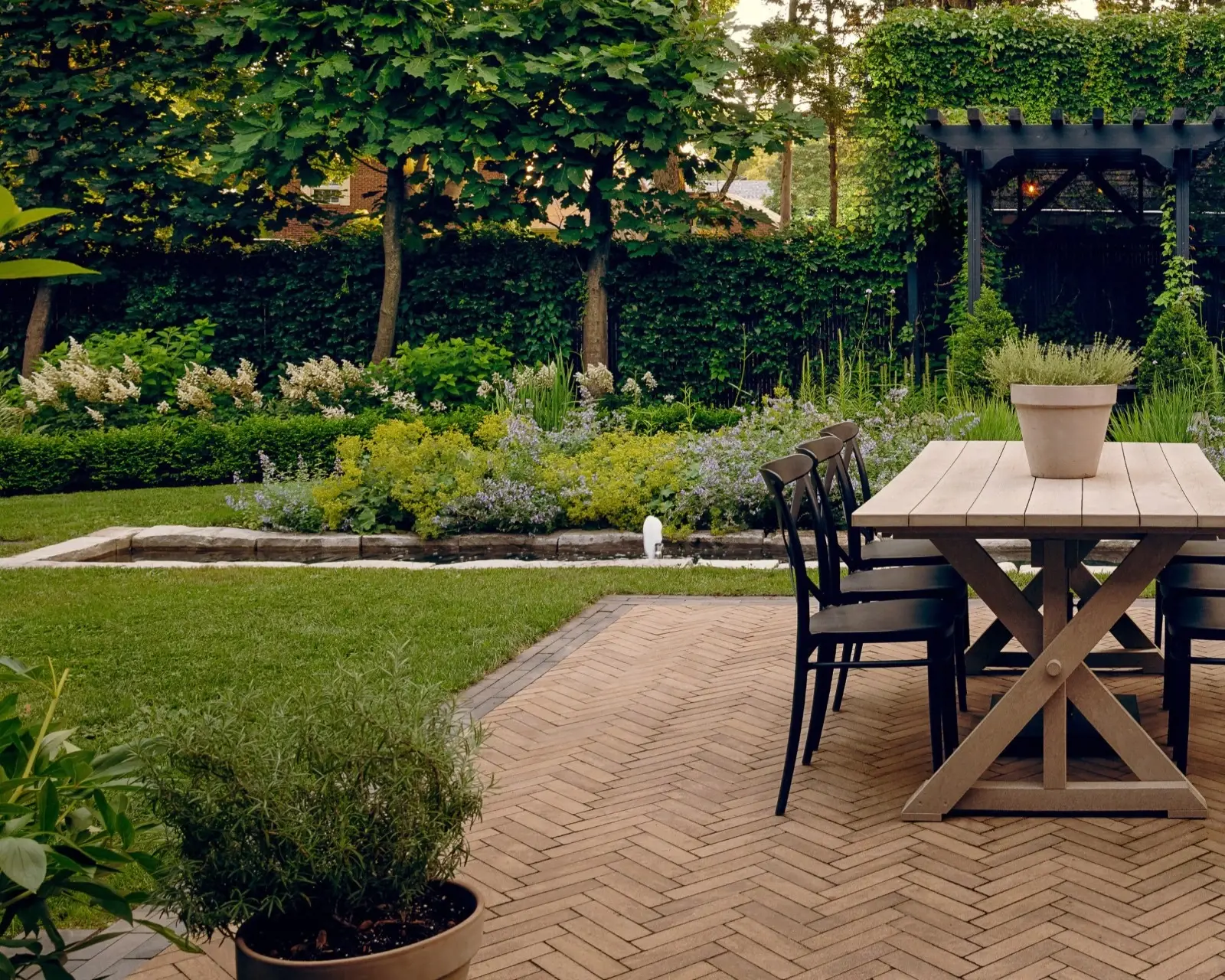 Outdoor dining area with Techo-Bloc Westmount pavers laid in a herringbone pattern, surrounded by greenery and garden structures.