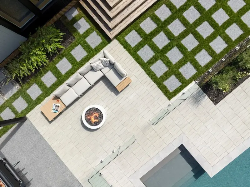 Modern backyard lounge area with Techo-Bloc Industria pavers, Terrazzo slabs, grass joints, outdoor sofa, fire feature, and poolside layout.