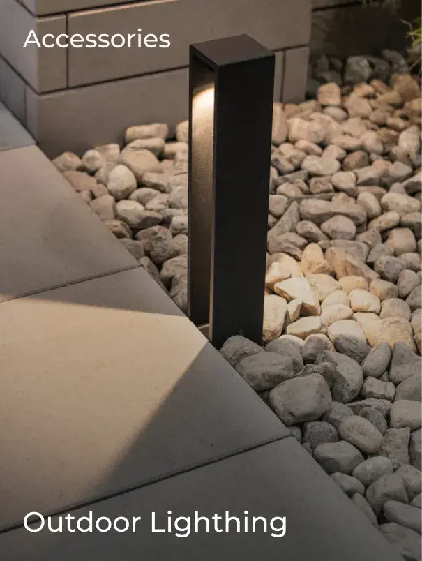 Modern black outdoor lighting fixture installed beside stone pavers and decorative river rock.
