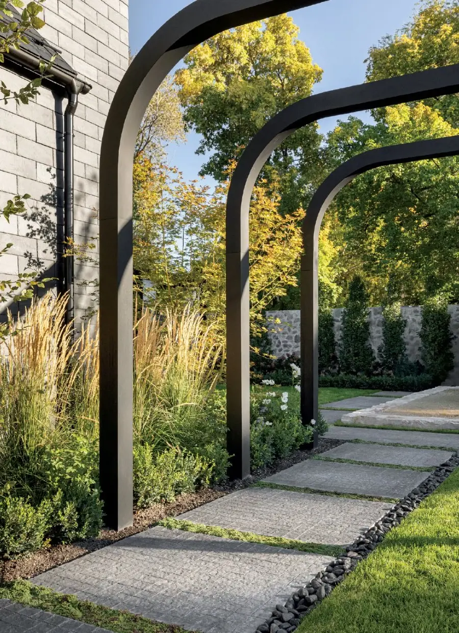 Garden pathway with concrete slabs, greenery, and curved architectural structures.