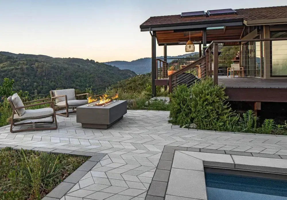 Contemporary patio with geometric paver layout, integrated fire feature, and comfortable seating overlooking a mountain landscape.