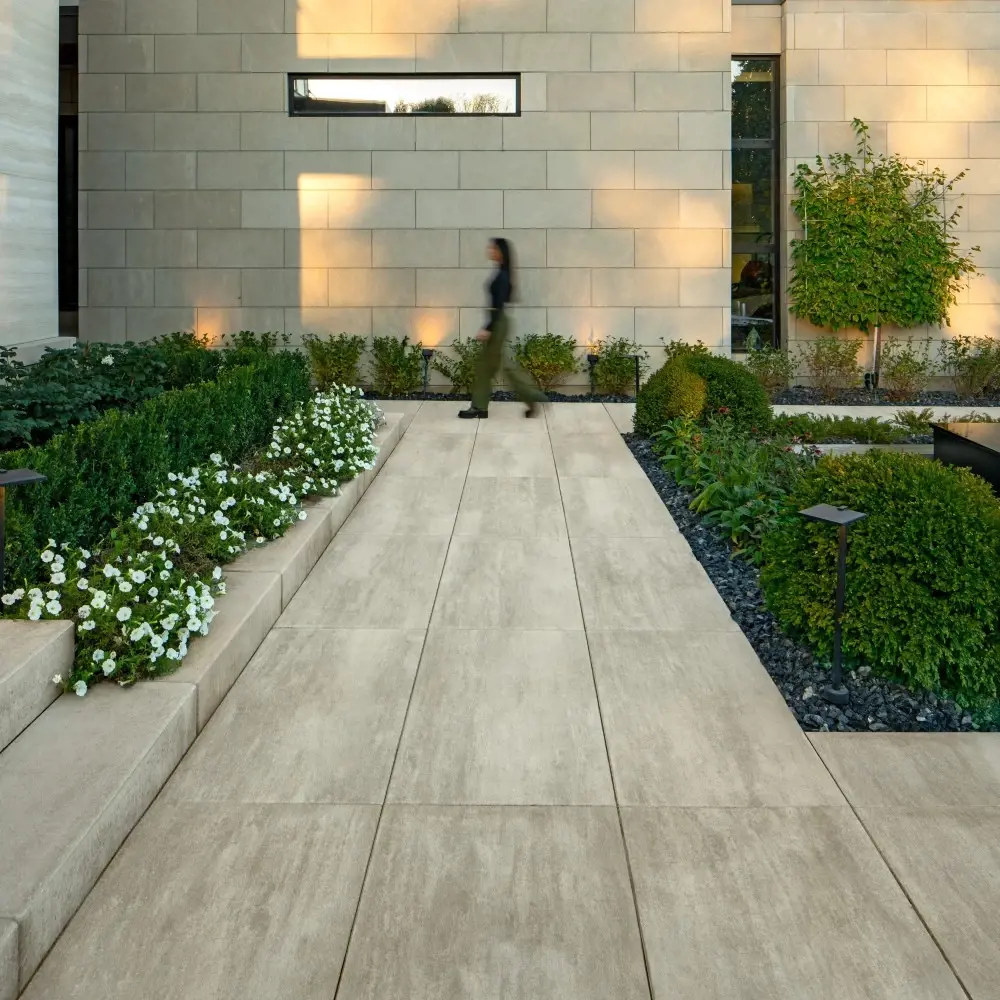 Allée de jardin avec des dalles de béton Industria 600 et 900 en Caffè Crema, encadrée par des massifs végétalisés et des lignes architecturales épurées.