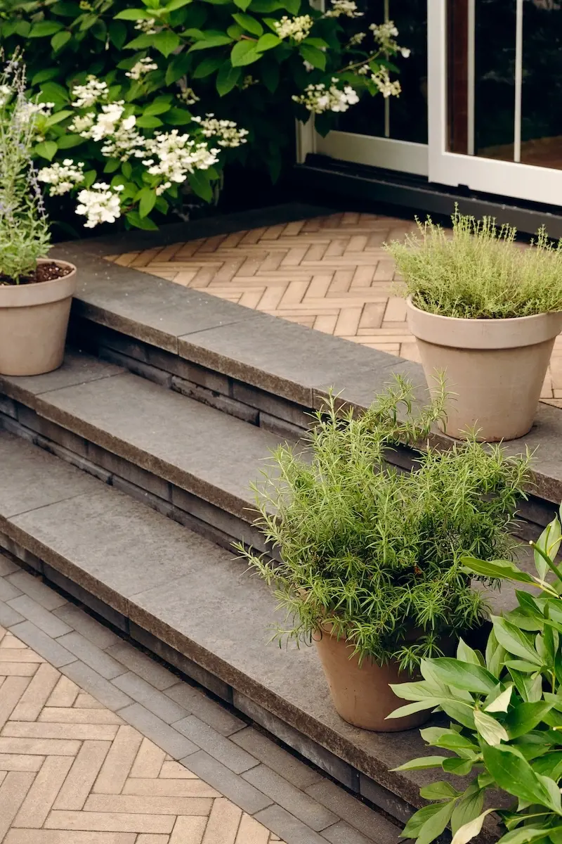 Backyard steps with Techo-Bloc Westmount pavers, Limestone cap detail, layered garden planting, planters, and a modern home entrance.
