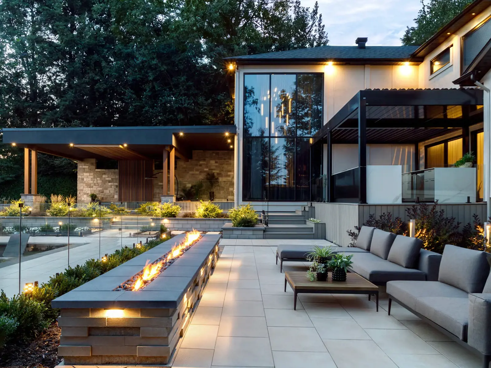 Modern backyard at dusk featuring a sleek fire feature, lounge seating, and illuminated contemporary landscaping.