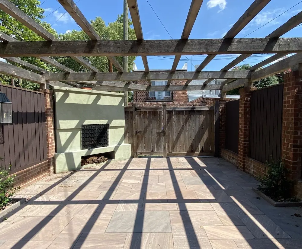 Photo avant d’une petite cour arrière urbaine avec d’anciens pavés de béton, une clôture en bois et une structure de pergola avant la rénovation du patio.