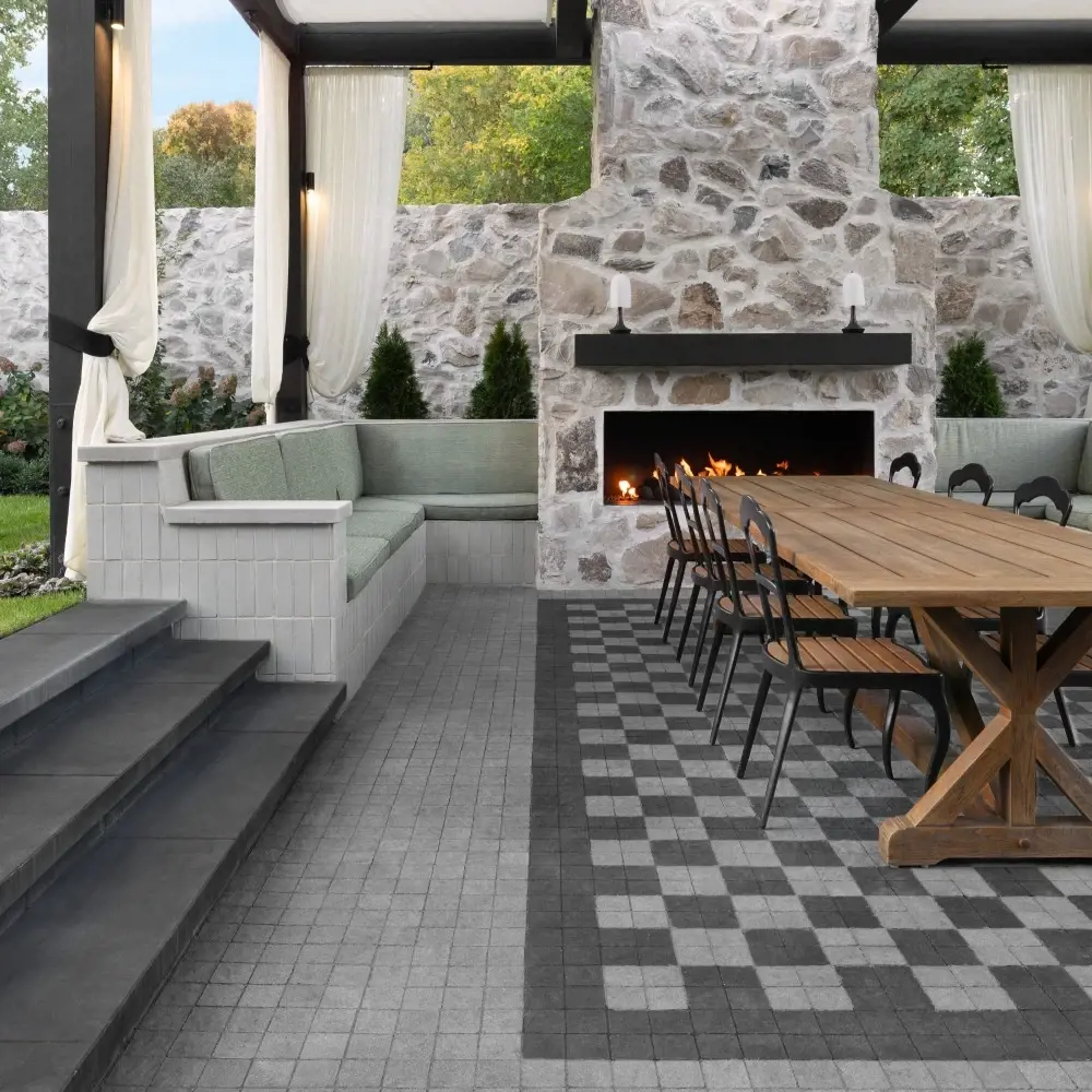 Outdoor dining area with Squadra concrete pavers in Onyx Black and Shale Grey, arranged in a contrasting pattern beside a stone fireplace.
