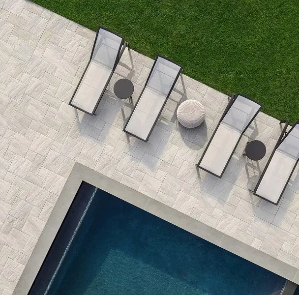 Terrasse au bord de la piscine avec chaises longues, petites tables et pelouse verte.