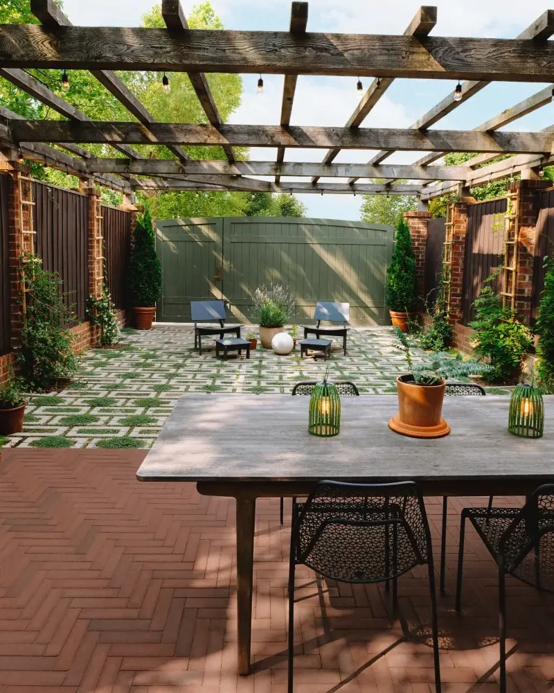 Outdoor courtyard featuring permeable pavers in a geometric pattern, surrounded by greenery and a wood pergola.