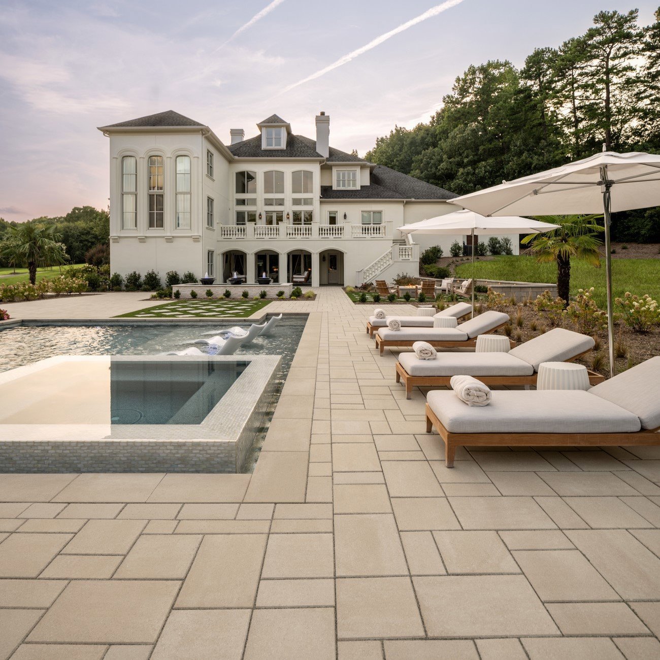 Blu 60 Smooth Slabs by Techo-Bloc in beige, modular patio around pool with cushioned loungers in front of grand mansion.