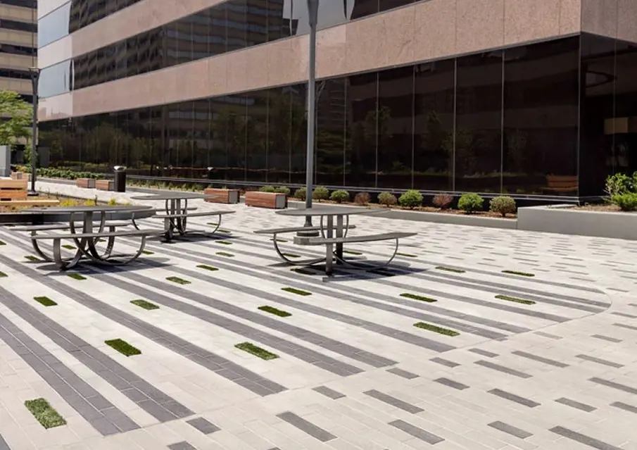 Place extérieure pavée avec les dalles Linea de Techo-Bloc en Greyed Nickel et Onyx Black, avec texture lisse et bandes végétales.