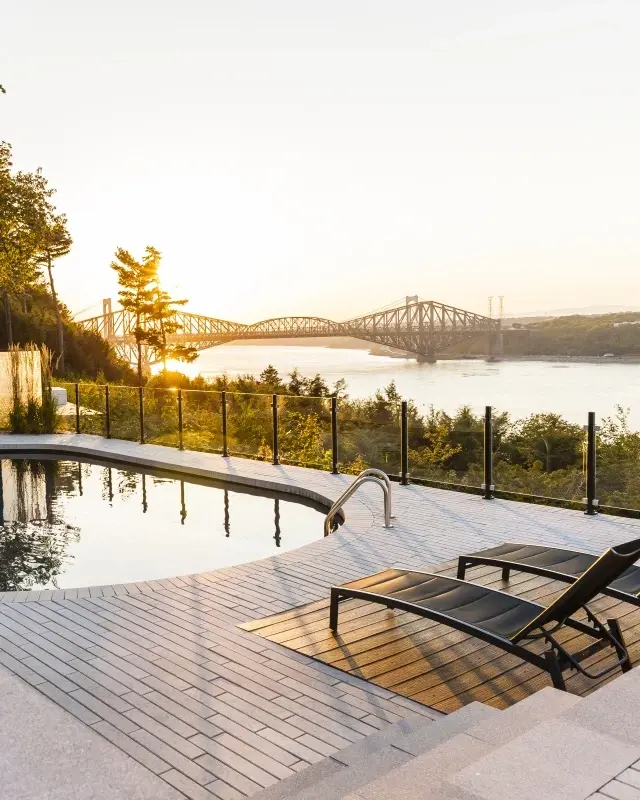 Industria slabs with Raffinato caps forming a sleek poolside patio overlooking a scenic river and bridge at sunset.