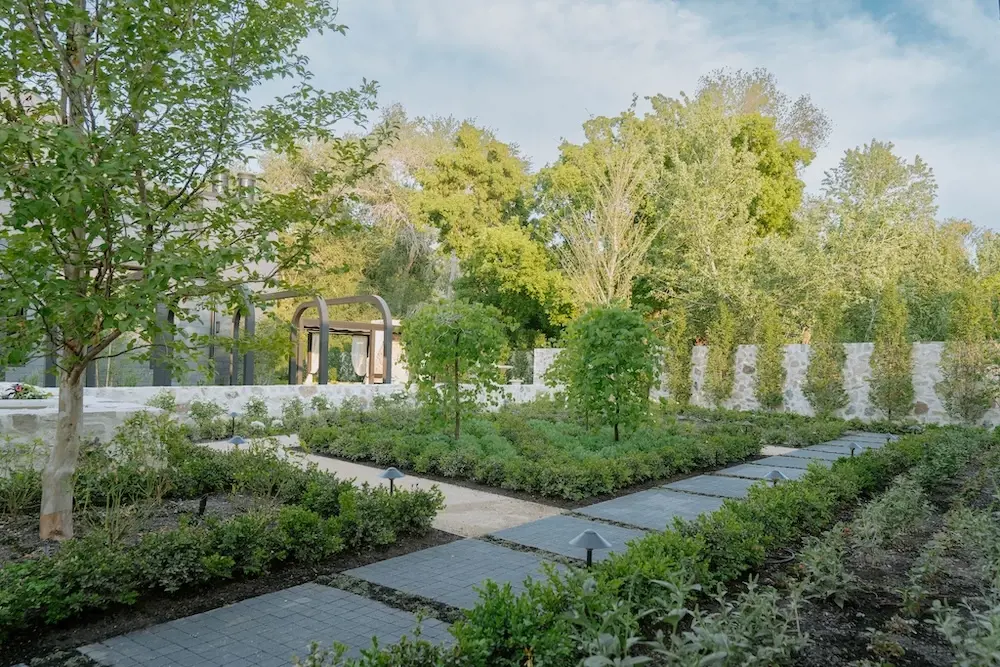Garden walkway with Techo-Bloc Squadra pavers, lush planting beds, stone walls, trees, and a quiet courtyard layout.