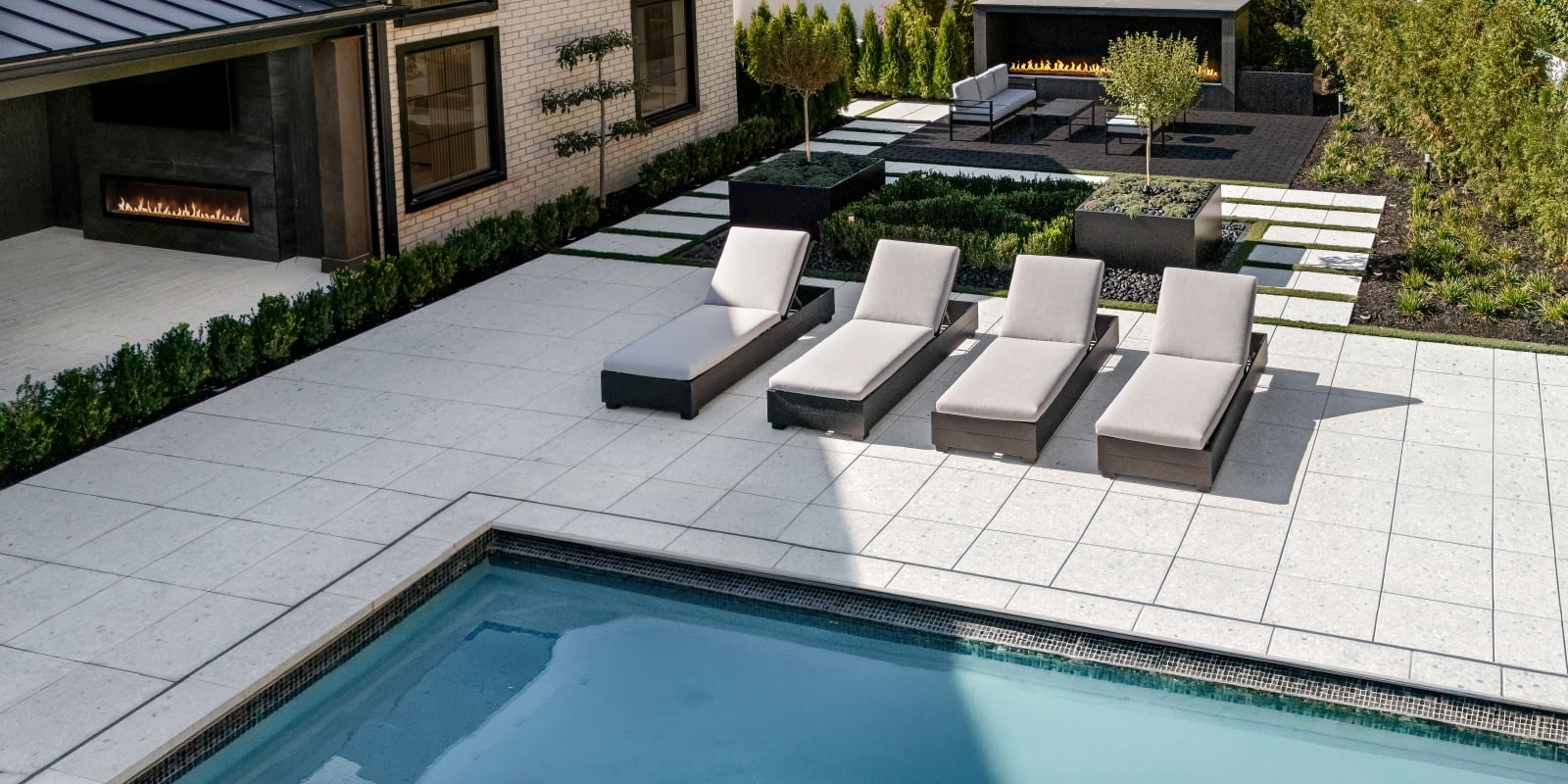 Terrazzo Slab in Mineral White creates a poolside patio with large paving stones and lounge chairs.