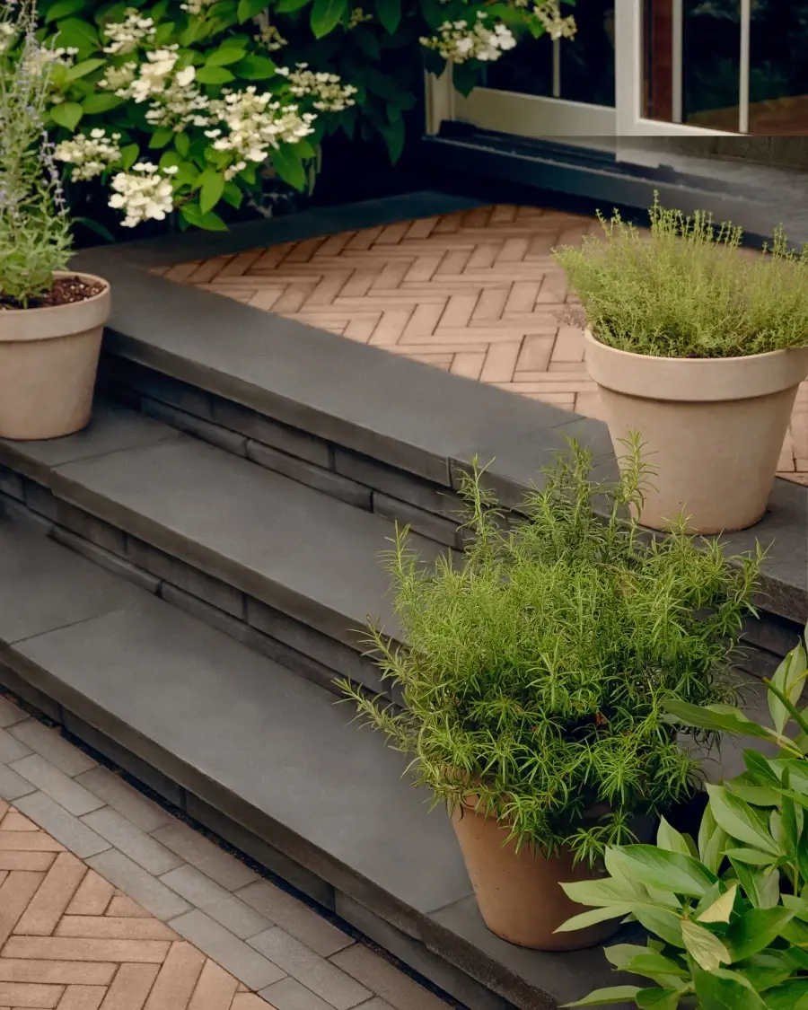 Garden steps built with Westmount cobblestone style pavers in Chestnut Brown and framed with limestone caps in Onyx Black, softened by layered greenery.