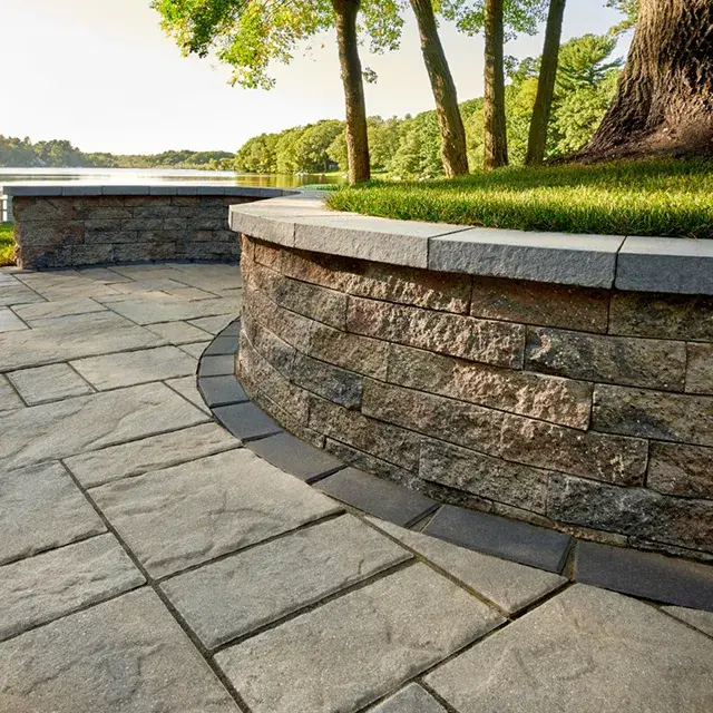 Mini-Creta Architectural by Techo-Bloc, concrete retaining wall blocks with clean edges, forming a curved wall along a patio for added structure and elegance.