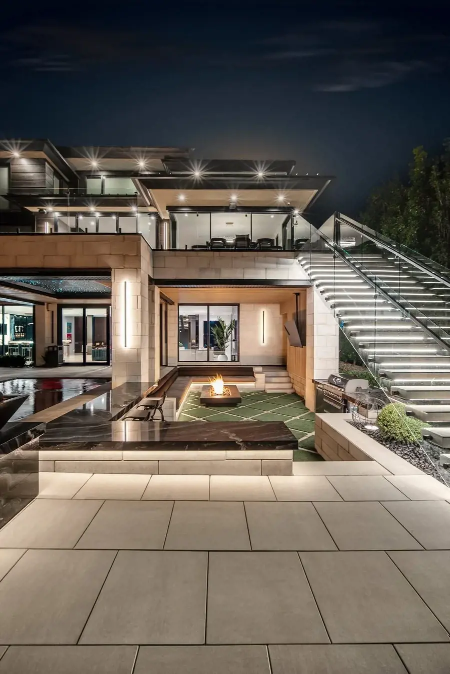 Illuminated outdoor entertainment area with fire feature, textured pavers, and modern lounge seating.