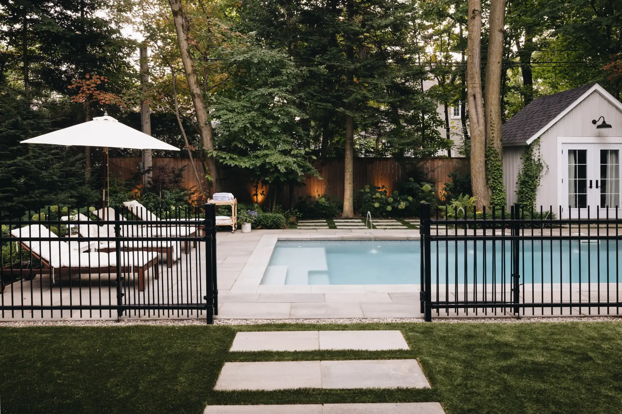 Terrasse en pavé et margelle de piscine près d'une clôture noire en métal et du gazon