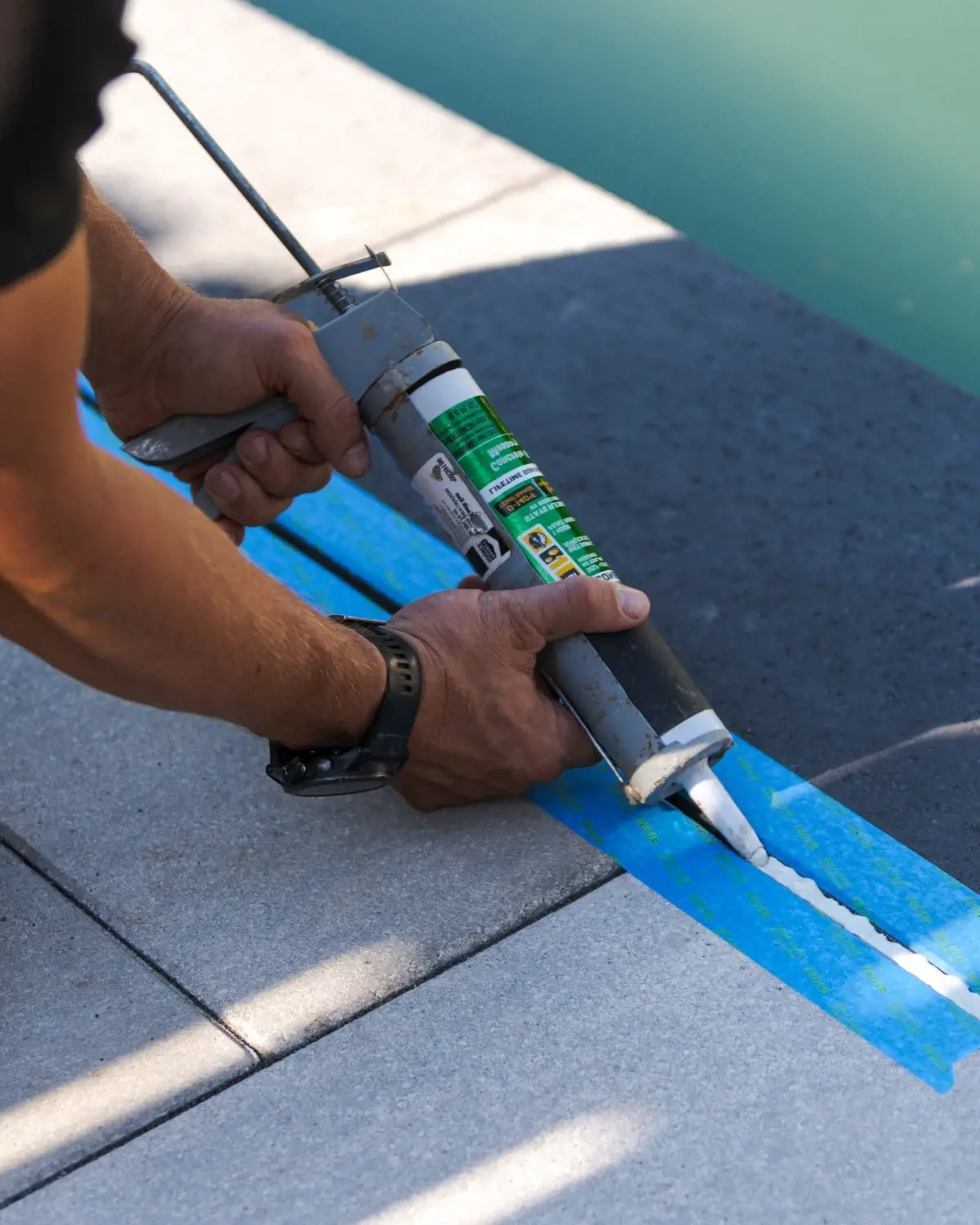 Contractor applying a waterproof liner or sealant with a caulking gun between permeable pavers.
