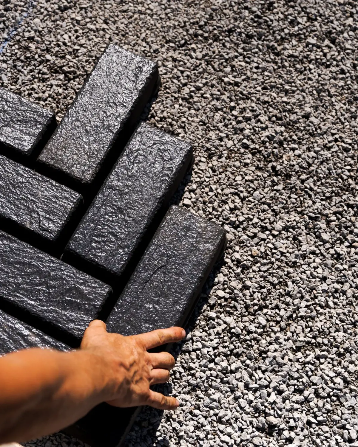 Contractor hand applying jointing material between dark pavers for a clean, durable finish.